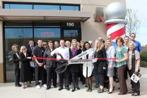Holding the Roseville Chamber ribbon cutting scissors is Toney Sebra, center, and his wife Megan Sebra, at right, owners of the Roosters Men's Grooming Center at Nugget Plaza.  They are joined by representatives of the Chamber, local community and Roosters' staff.