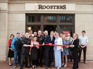 Tyson White, owner of Roosters Men's Grooming Center in Boston, at center, prepares for the store's ribbon cutting with wife Alexandra DaCosta, at right, along with representatives of local businesses, neighbors and Roosters' team members.